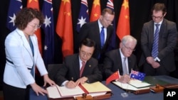 Australian Prime Minister Tony Abbott, back center, watches as China's Minister of Commerce Gao Hucheng, second left, and Australian Minister for Trade Andrew Robb, second right, sign a free trade agreement between the two countries in Canberra, Australia