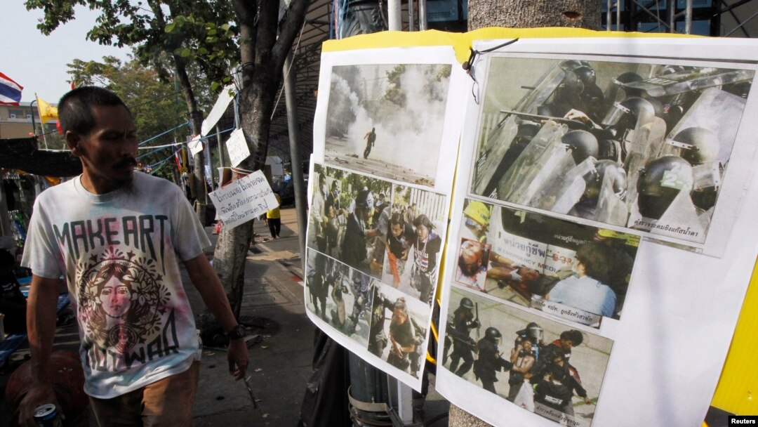 An anti-government protester walks past pictures taken during clashes with riot policemen, during a rally outside the Government House in Bangkok December 29, 2013.