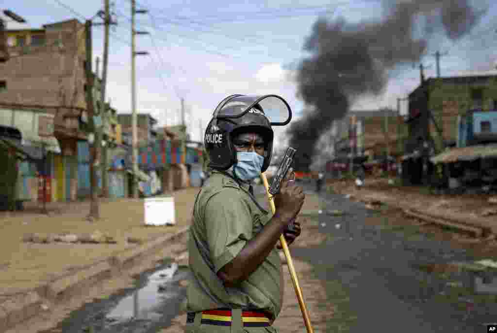 A police officer holds a pistol during clashes with protesters near a burning tire barricade in the Kariobangi slum of Nairobi, Kenya.