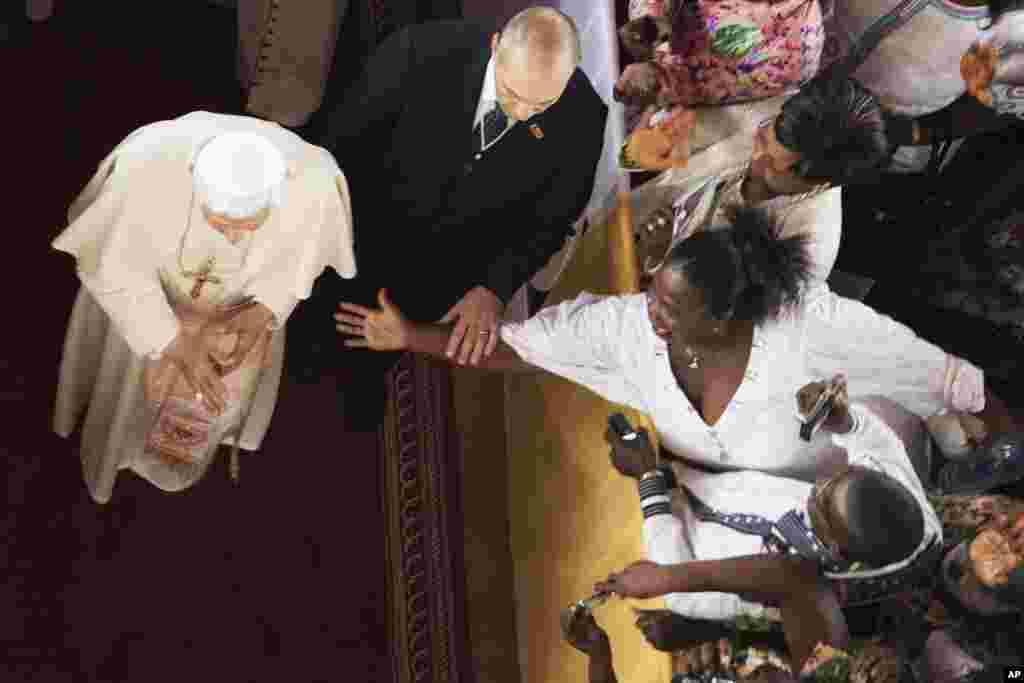A body guard (C) for Pope Benedict XVI deflects the hand of a woman reaching towards the pontiff as he leaves the Basilica in the city of Ouidah in Benin, November 19, 2011. Pope Benedict said on Saturday the developed world could not continue to look dow
