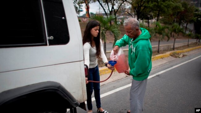 Una mujer sostiene un embudo y una manguera mientras un hombre llena su tanque después de quedarse sin gasolina en Caracas, Venezuela, el jueves 23 de marzo de 2017.