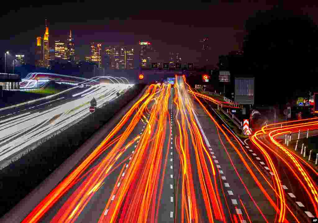 A long exposure photo shows cars and trucks driving on a highway towards the skyline in Frankfurt, Germany.