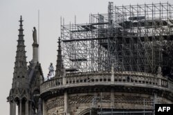 Workers stand on the roof of the Notre Dame de Paris cathedral in Paris on April 23, 2019, one week after a fire devastated the cathedral (Photo by Christophe ARCHAMBAULT / AFP)