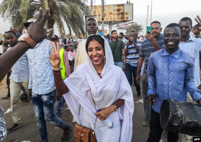 FILE - Alaa Salah flashes the victory gesture and shouts slogans while marching during a demonstration in front of the military headquarters in the capital Khartoum, April 10, 2019.