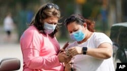In this file photo, women wear masks as they check a mobile phone Wednesday, July 1, 2014, in Houston, Texas. (AP Photo/David J. Phillip)