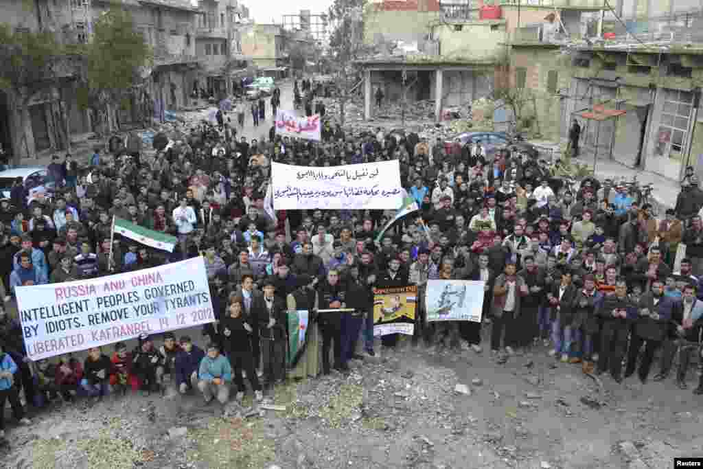 Demonstrators hold banners near damaged buildings during a protest against Syria's President Bashar al-Assad, after Friday prayers in Kafranbel near Idlib December 14, 2012. REUTERS/Raed Al-Fares/Shaam News Network/Handout (SYRIA - Tags: CIVIL UNREST MILI