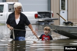 FILE - Richard Rossi and his 4-year-old great grandson, Justice, wade through water in search of higher ground after their home took in water in St. Amant, Louisiana, Aug. 15, 2016