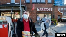 Seorang pria mengenakan masker wajah membawa berkotak-kotak rokok yang dibelinya di perbatasan Macquenoise setelah Perancis membuka perbatasan dengan negara tetangga setelah pencabutan lockdown untuk mencegah penularan Covid-19, di Macquenoise, Belgia, 15 Juni 2020.