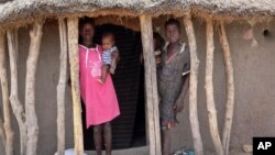 Children stand in the doorway of their home as they watch their mother prepare food she received from an aerial food drop by the World Food Program in the town of Kandak, South Sudan, May 2, 2018. 