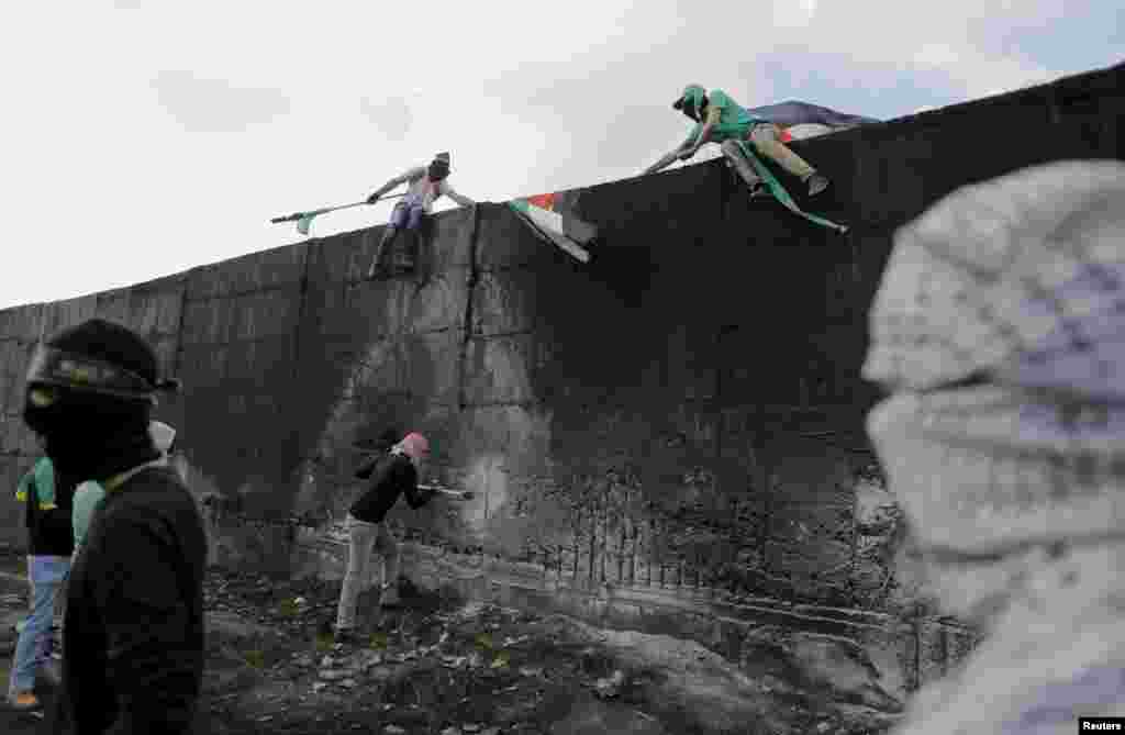 A Palestinian protester tries to hammer a hole through the Israeli barrier that separates the West Bank town of Abu Dis from Jerusalem, as others climb on the barrier during clashes with Israeli troops.