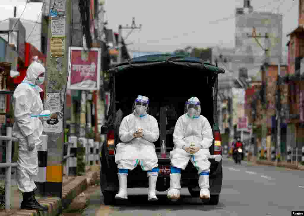 Members of Nepal army personnel wearing personal protective equipment (PPE) rest on a vehicle as they wait to transport a body of a person who died from COVID-19 to the crematorium in Kathmandu.