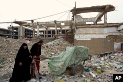 Homeless Iraqi people push their belongings through the rubble of al-Rashid military base belonging to the former Iraqi army in Baghdad, Iraq, Feb. 12, 2018.