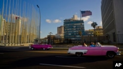 FILE - Tourists ride in classic American convertible cars past the United States embassy, right, in Havana, Cuba, Jan. 12, 2017.
