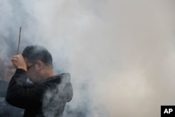 A Chinese man is covered by incense smoke as he offers prayers on the first day of the new year at Beijing's Yonghegong Lama Temple as the Chinese capital is blanketed by heavy smog, Jan. 1, 2017.