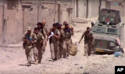 FILE - This frame grab from video released July 4, 2017, and provided by Furat FM, a Syrian Kurdish activist-run media group, shows U.S.-backed Syrian Democratic Forces fighters in the eastern side of Raqqa, Syria.