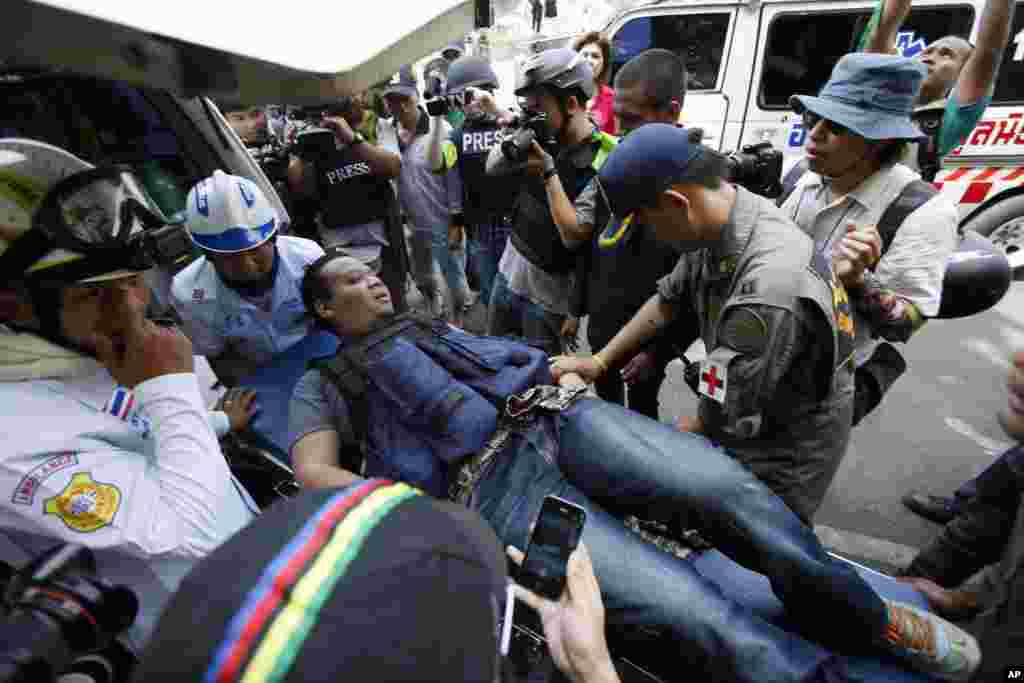 A local journalist is carried away by medics after being wounded from an explosive thrown towards riot police trying to retake a protest site in Bangkok, Feb. 14, 2014.