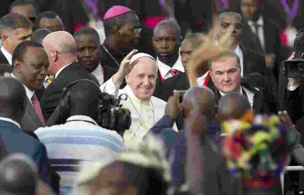 Pope Francis, center, waves to traditional dancers accompanied by Kenya's President Uhuru Kenyatta, left on his arrival at the airport in Nairobi, Nov. 25, 2015.