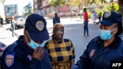 Une femme aspergée de gaz poivré par un membre du Service de police sud-africain (SAPS) pour ne pas avoir porté de masque facial en public, à Hillbrow, Johannesburg, le 1er mai 2020. (Photo AFP/Michele Spatari)