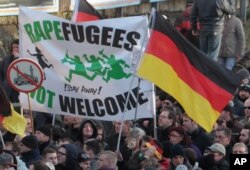 FILE - Demonstrators hold a sign that reads "Rapefugees not welcome! Stay away!" and a sign with a crossed out mosque as they march in Cologne, Germany, Jan. 9, 2016.