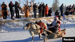 A contestant wearing a Santa Claus costume rides in a sledge pulled by a reindeer during a race on snow-covered tracks at the opening ceremony of a local winter festival in Genhe of Hulun Buir, north China's Inner Mongolia Autonomous Region, December 24,