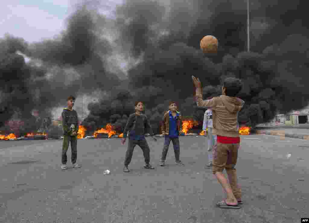 Children play with a ball on a street blocked with burning tires, amid a general strike in the southern city of Basra, Iraq.