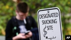 FILE - A University of Washington student smokes at one of a handful of designated smoking locations on the campus Tuesday, Oct. 27, 2015, in Seattle. (AP Photo/Elaine Thompson)