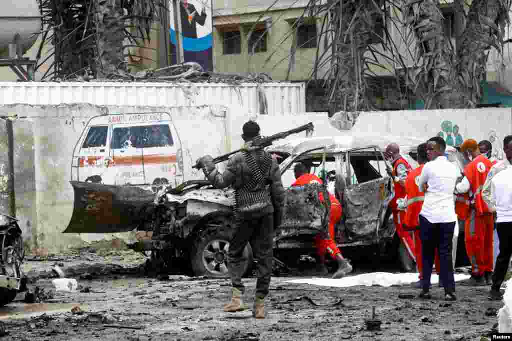 A police officer keeps watch as Red Crescent workers remove the body of a victim at the scene of a suicide car bomb explosion near the president&#39;s residence, in Mogadishu, Somalia, Sept. 25, 2021.