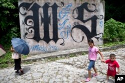 FILE - a family walks by a wall covered by a symbol from the Mara Salvatrucha, of MS-13 gang in Ilopango, El Salvador.