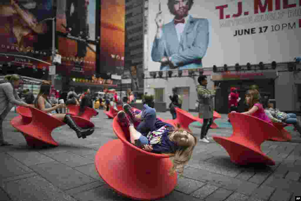 Para pengunjung menikmati suasana di Times Square, New York dengan duduk di kursi yang bisa berputar.