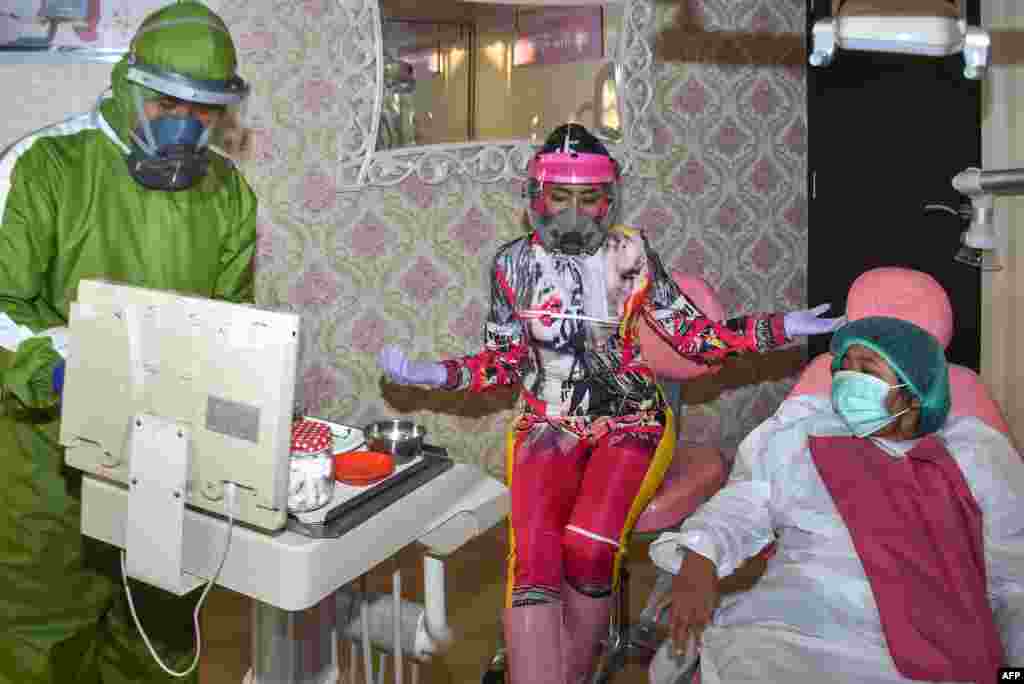 Dentist Nina Agustin (C) and her assistant (L) wearing figured Personal Protective Equipment (PPE) prepare to examine their patient at a clinic, in Malang, East Java province, Indonesia, July 27, 2020. 