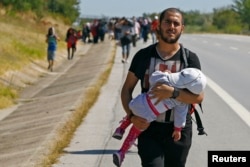 FILE - A Syrian migrant carries a baby as he walks towards the Greece border on a road near Edirne, Turkey, Sept. 15, 2015.