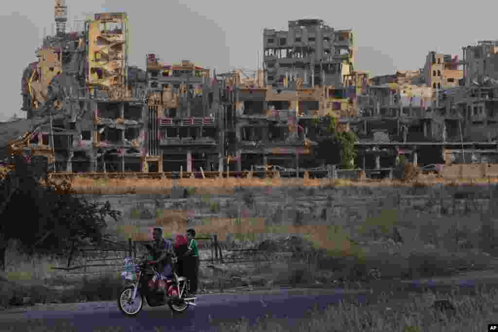 People ride their motorcycle by damaged buildings in the old town of Homs, Syria, Aug. 15, 2018.