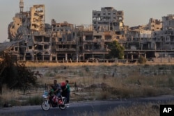 FILE - People ride their motorcycle by damaged buildings in the old town of Homs, Syria, Aug. 15, 2018. Turkish President Recep Tayyip Erdogan earlier this month unveiled plans for major housing projects in a proposed Turkish-controlled military security zone in Syria.