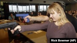 FILE - Clark Aposhian demonstrates with a plastic gun, rear, while Joanna Baginska, a fourth-grade teacher from Odyssey Charter School, in American Fork, Utah, aims a handgun during concealed-weapons training training.