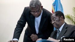 FILE - Congolese Justice Minister Alexis Thambwe Mwamba, right, is assisted by Abbot Donatiuen N'shole, CENCO secretary general, as he signs the accord between the opposition and the government of President Joseph Kabila at CENCO headquarters in Kinshasa, Dec. 31, 2016. 
