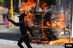 A protesting student runs past a burning bus off campus outside the University of the Witwatersrand in Johannesburg, South Africa on Monday, Oct. 10, 2016. (AP Photo)