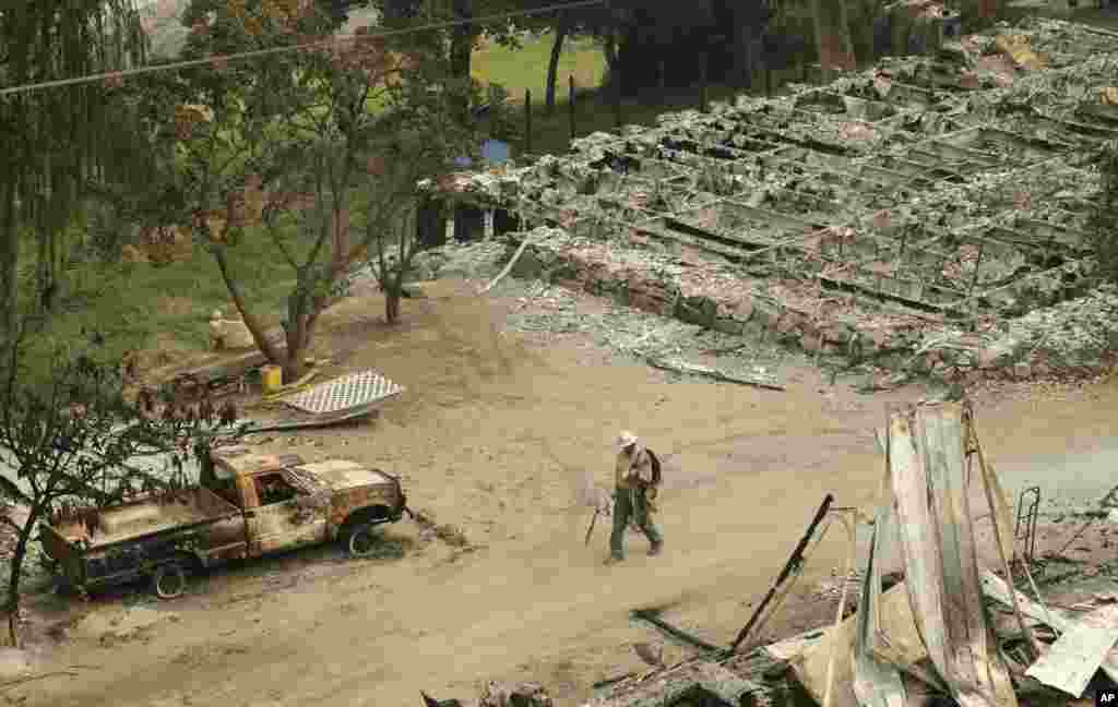 A Chelan County Public Utility District worker walks past a burned structure along State Route Alt. 97 highway outside of Chelan, Washington, Aug. 17, 2015. Big wildfires threatened the Lake Chelan resort region of central Washington after driving away tourists, destroying a warehouse filled with nearly 2 million pounds of apples and forcing thousands of residents to flee.