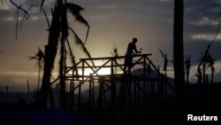 A man is silhouetted as he builds a wooden house in an area destroyed by Typhoon Haiyan, in Palo November 19, 2013. 