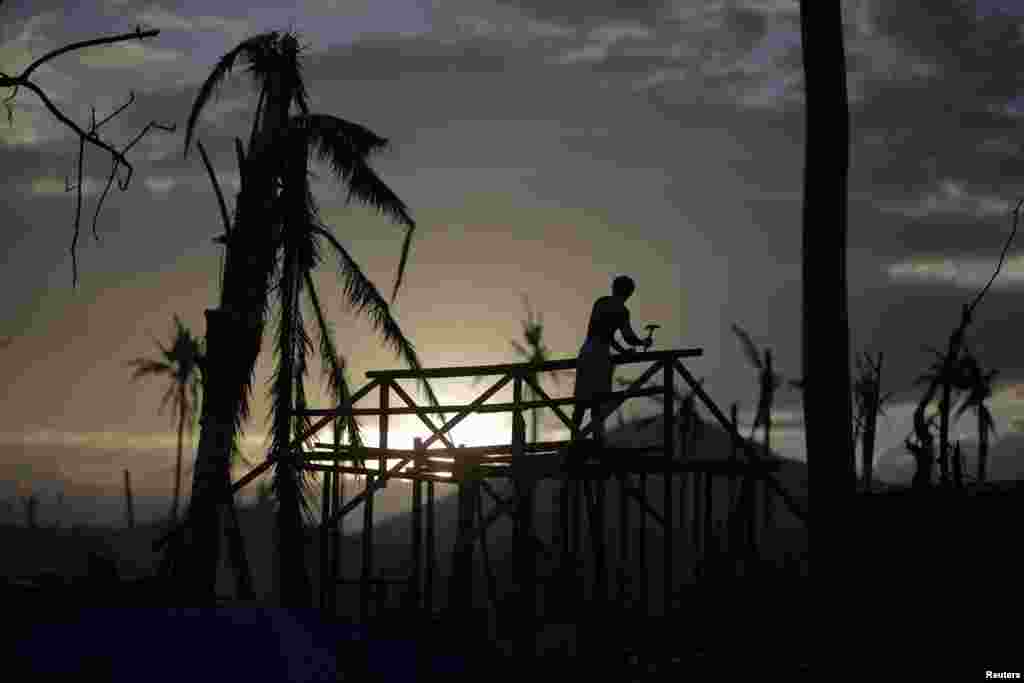 A man is silhouetted as he builds a wooden house in an area destroyed by Typhoon Haiyan, in Palo, Philippines.