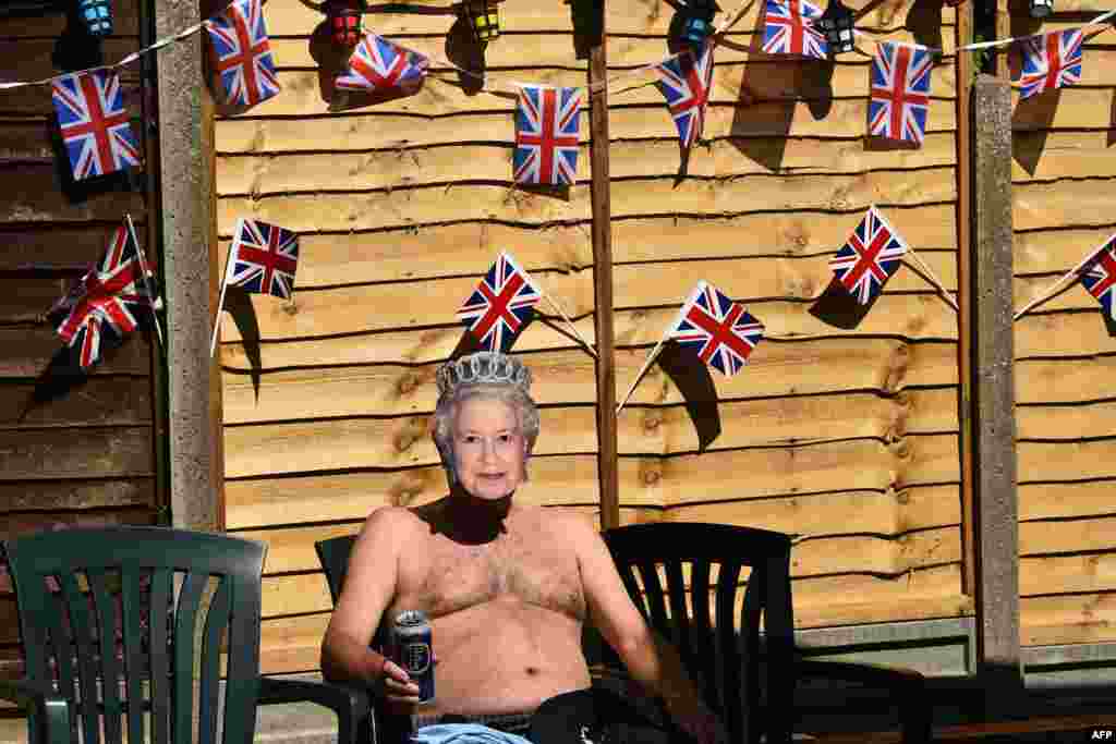 Terry Livesey, wearing a mask of Britain&#39;s Queen Elizabeth II, sunbathes in his garden surrounded by Union flags as people mark the 75th anniversary of Victory in Europe Day, the end of the Second World War in Europe in Portslade, southern England. 