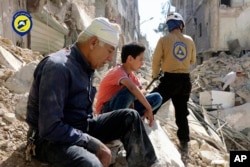 In this picture provided by the Syrian Civil Defense group known as the White Helmets, residents sit amongst rubble in rebel-held eastern Aleppo, Syria, Oct. 11, 2016.