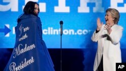 Hillary Clinton aplaude a la artista Katy Perry al subir al escenario de un mitin en Filadelfia. Su capa tiene un letrero que dice: "Apoyo a la señora presidenta".