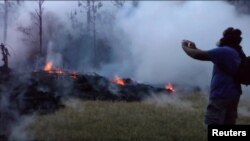 A man wearing a gas mask takes pictures of a lava fissure in Leilani Estates, Hawaii, May 9, 2018, in this still image taken from a social media video. 