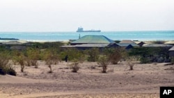 A lone figure makes its way past the bushes in the outskirts of the central Somali coastal town of Hobyo as the outline of a hijacked ship is seen anchored off the coast (File)