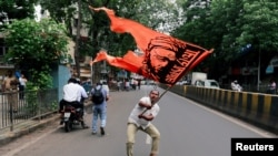 FILE - A man waves a flag as he blocks a road during a protest, organized by Maharashtra state's Maratha community, to press their demands for reserved quotas in government jobs and college places for students in Mumbai, India, July 25, 2018. 