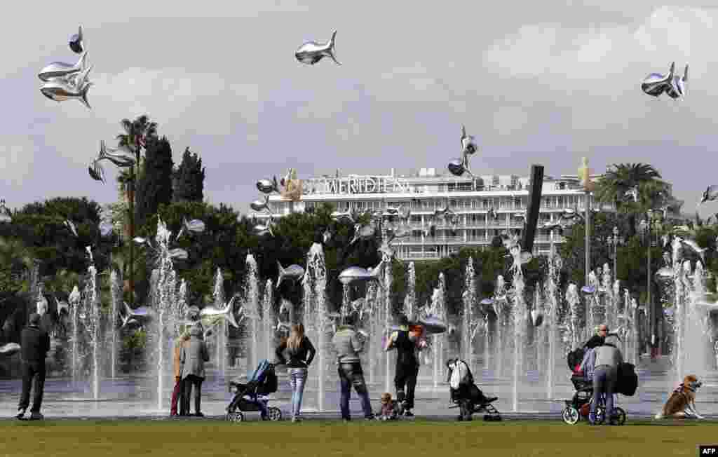 People look at fish-shaped balloons in front of water fountains in Nice on the French Riviera.