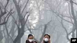Chinese women wearing masks for protection against air pollution walk through Ritan Park shrouded by dense smog in Beijing, Dec. 19, 2016.