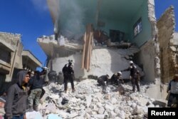 FILE - People and civil defense personnel remove rubble as they look for survivors at a damaged site after an airstrike on rebel-held Idlib city, Syria, March 19, 2018.
