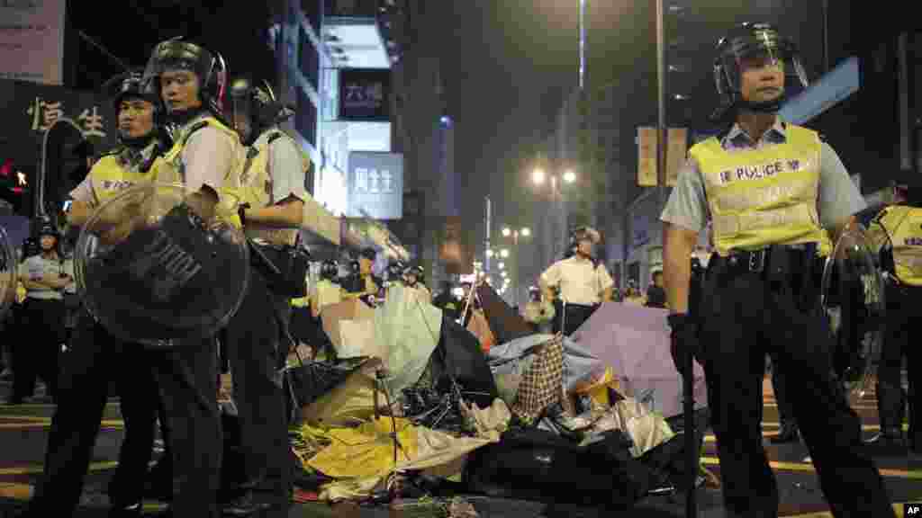 Riot police stand guard next to broken umbrellas used by protesters to protect themselves at a pro-democracy protest encampment in the Mong Kok district of Hong Kong, Oct. 19, 2014. 