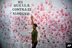 A woman poses in front of hand prints on a wall during an event against U.S. trade embargo against Cuba in Havana, Oct. 31, 2018. The United Nations voted Nov. 1 on a resolution regarding the ongoing U.S. trade embargo against Cuba.